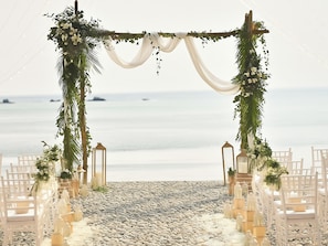 A beach wedding setup with a white aisle, floral decorations, and lanterns. - Grecotel Filoxenia Kalamata (Kalamata)