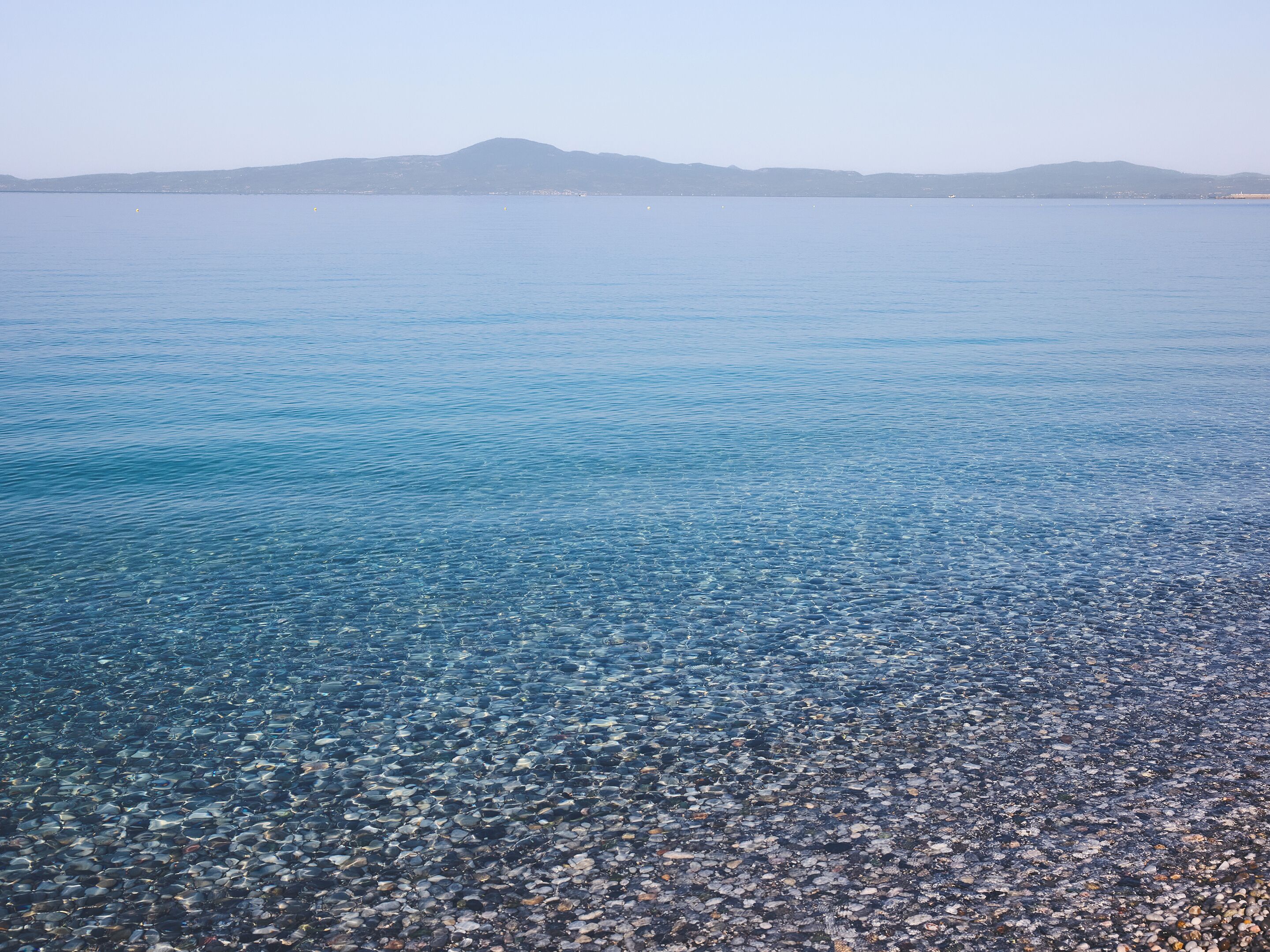 A clear view of a pebble beach leading into calm waters with distant mountains.