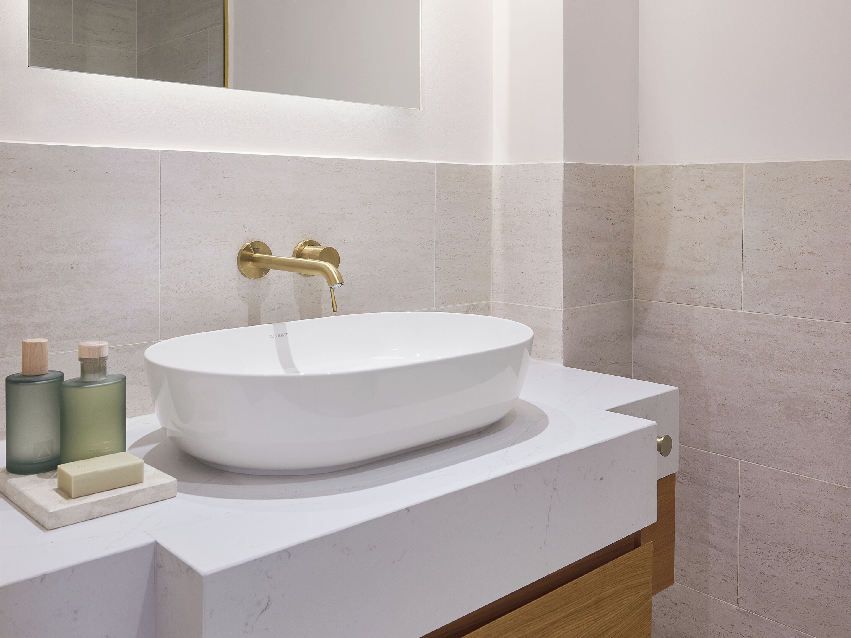 A modern bathroom with a white sink, gold faucet, and marble tiles.