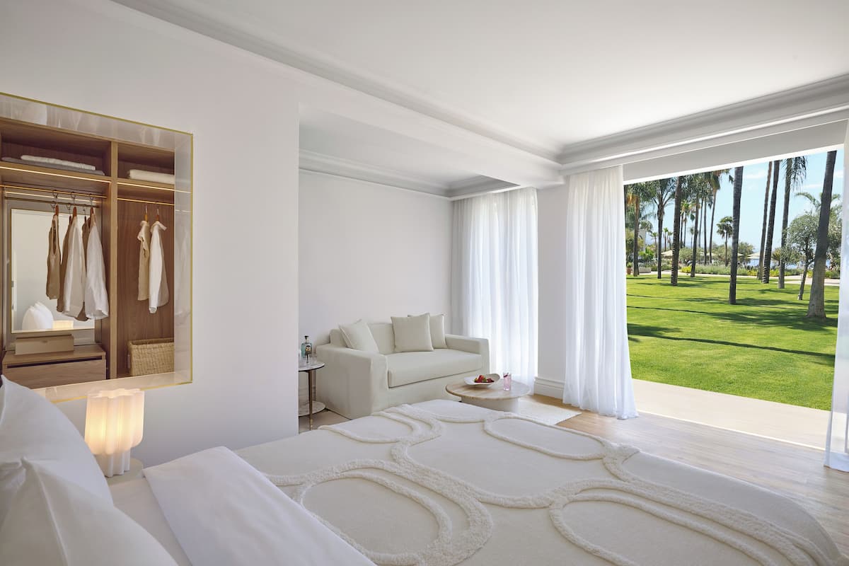 Une chambre d’hôtel avec un lit, un canapé, un miroir, une petite table et une vue sur un paysage verdoyant.