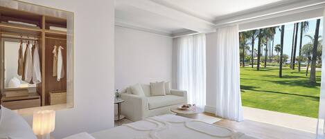Habitación de hotel con cama, sofá, espejo, mesita y vista a un paisaje verde.