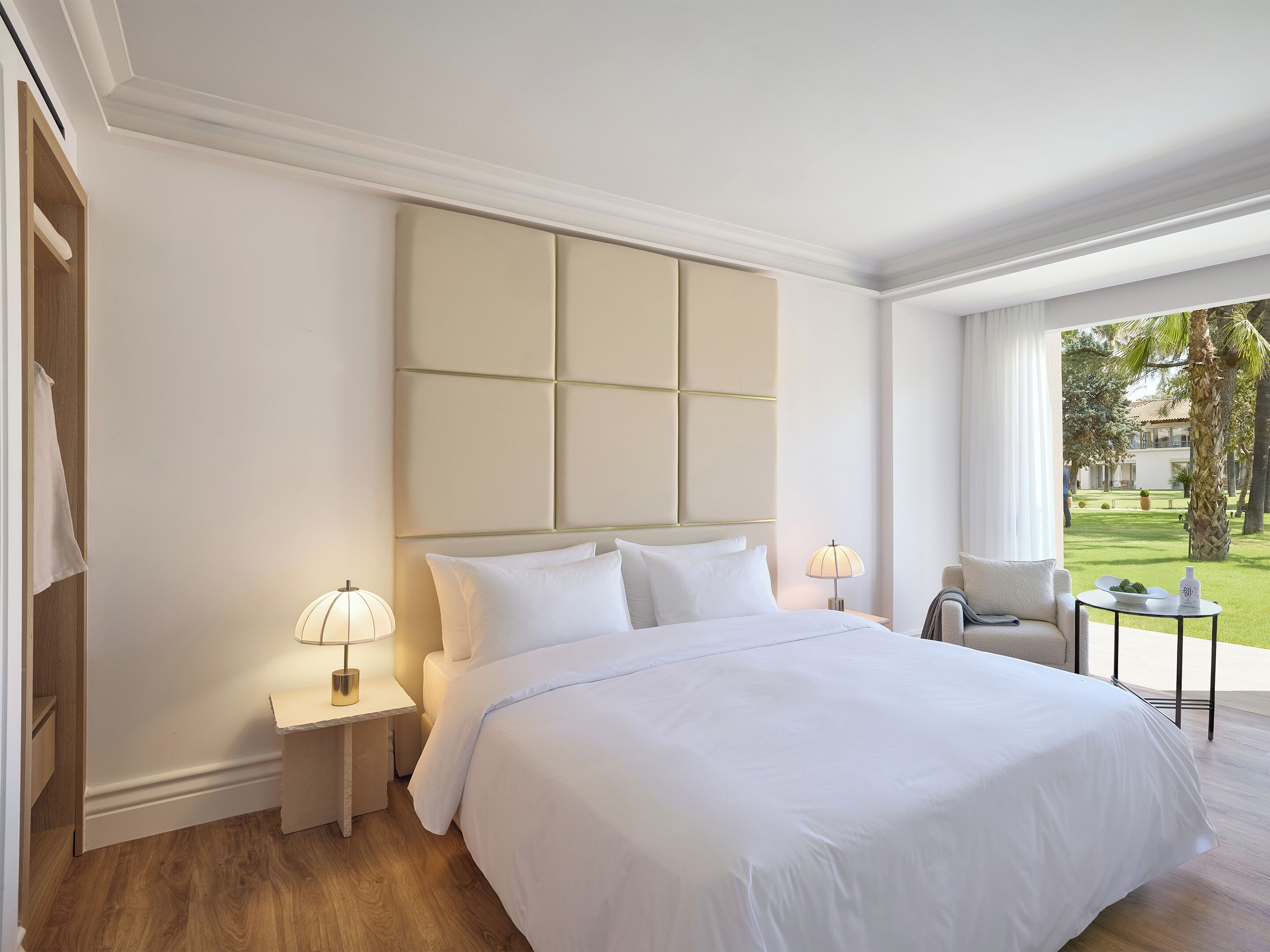 A hotel room with a large bed, two bedside tables, a chair, and a view of the garden.