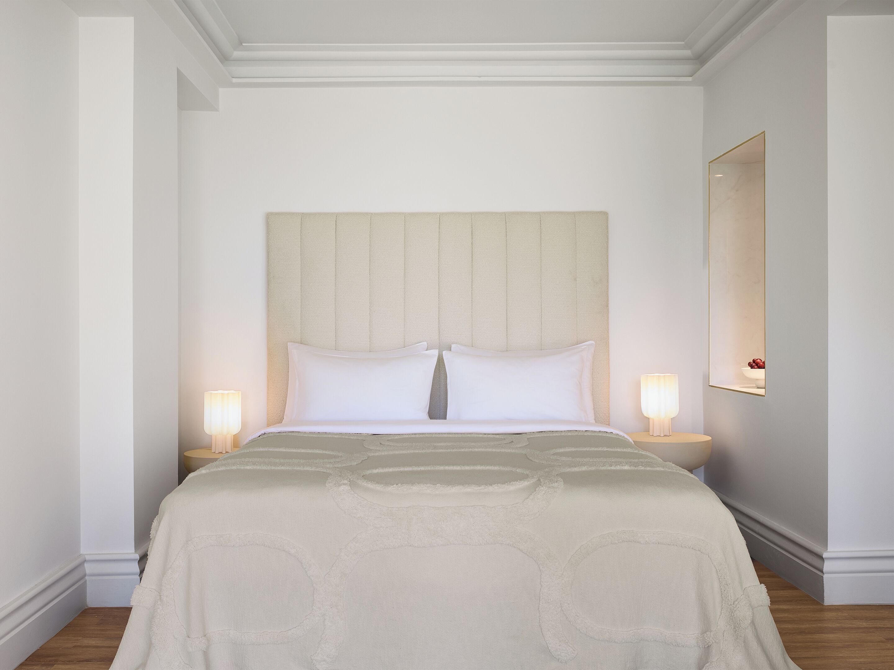 Een opgemaakt bed met hoofdeinde, twee bedlampen en een grote spiegel aan de muur.