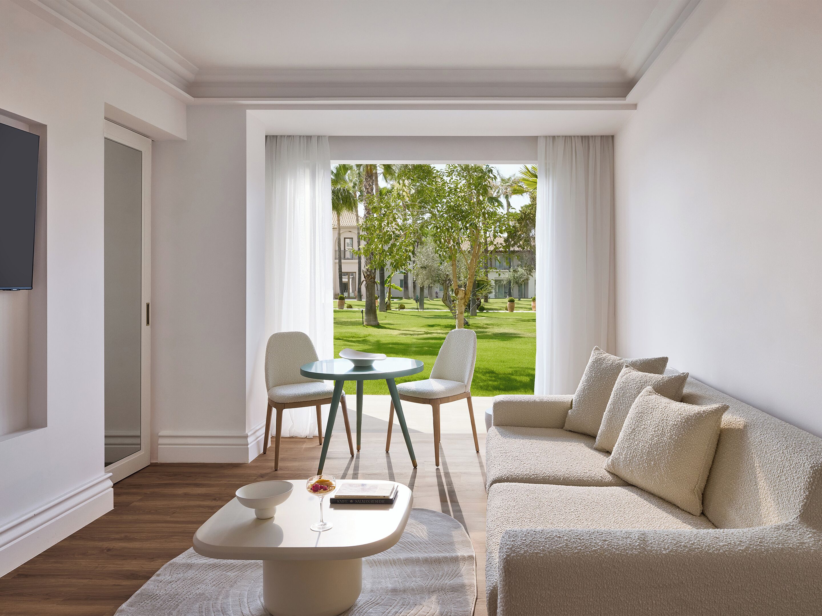 Habitación de hotel moderna con sofá, una mesa de comedor y vistas a un jardín bien cuidado.