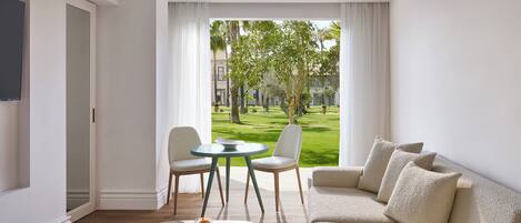 Habitación de hotel moderna con sofá, una mesa de comedor y vistas a un jardín bien cuidado.