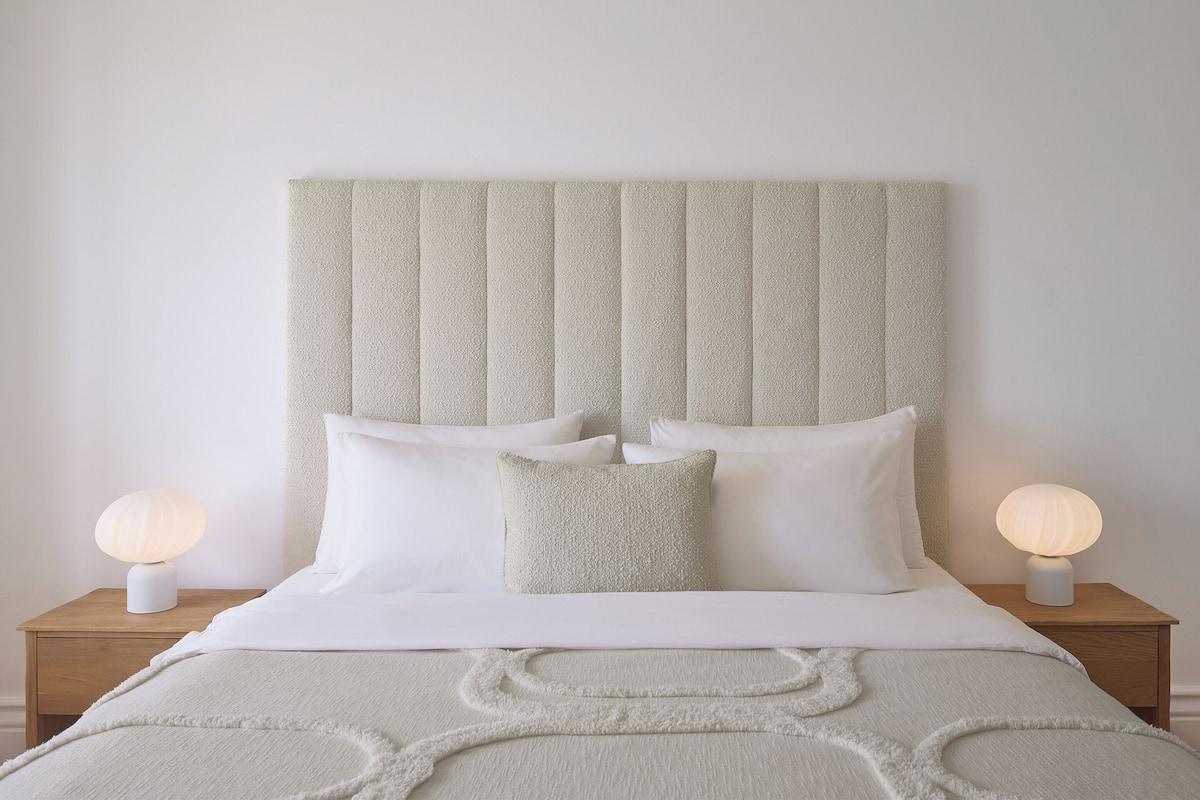 Une chambre à coucher avec un grand lit, deux tables de chevet avec des lampes et une tête de lit texturée.