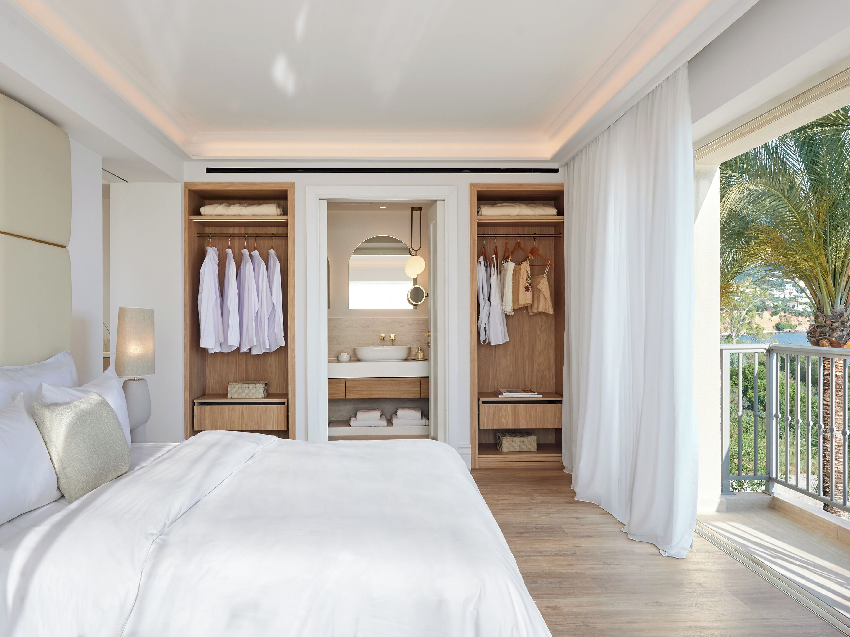 Ein Hotelzimmer mit einem großen Bett, einem begehbaren Kleiderschrank, einem Badezimmer mit Waschtisch und einem Balkon mit Aussicht.