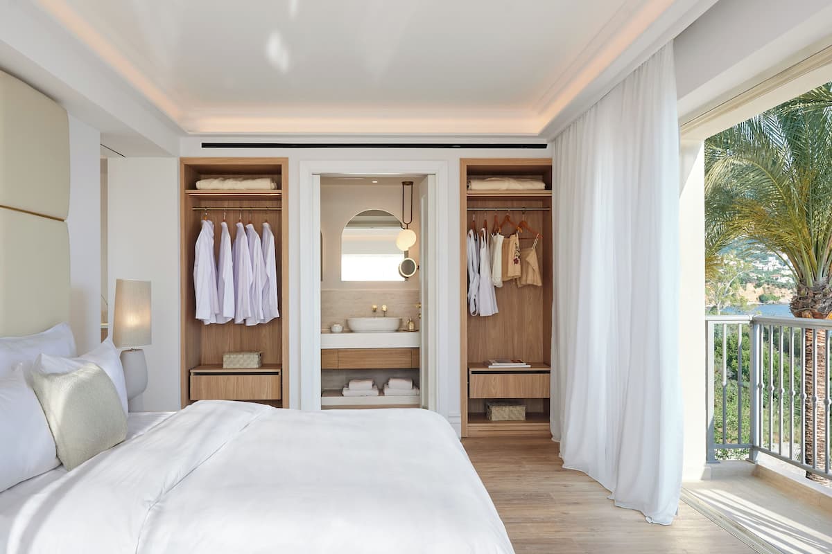 Une chambre d’hôtel dotée d’un grand lit, d’un dressing, d’une salle de bain avec un meuble-lavabo et d’un balcon avec vue.