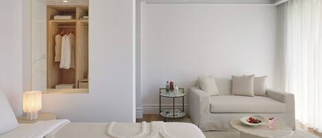 Un dormitorio minimalista con cama, sofá, una mesa de centro y un espejo que refleja un armario.