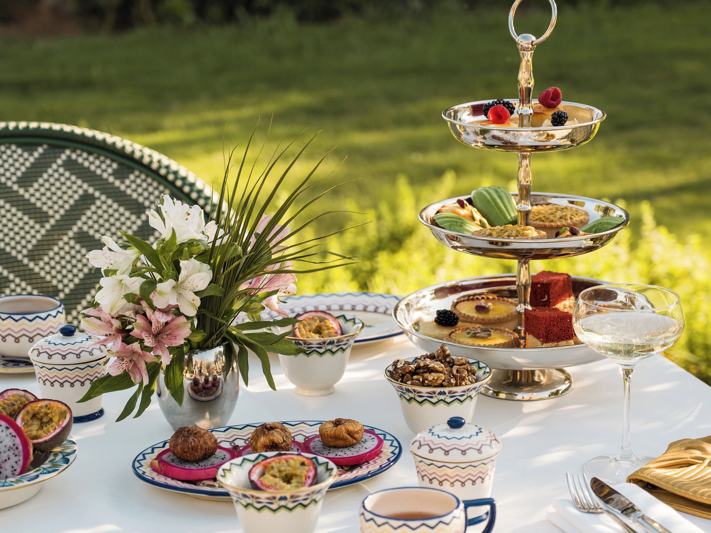 Une table dressée pour un repas, avec différents plats, un présentoir à gâteaux à plusieurs niveaux et un arrangement floral.