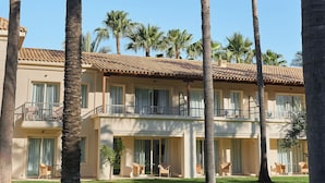 A multi-story hotel with balconies, palm trees, and a well-maintained lawn.