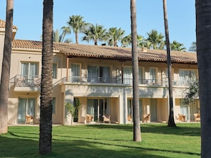 A multi-story hotel with balconies, palm trees, and a well-maintained lawn.