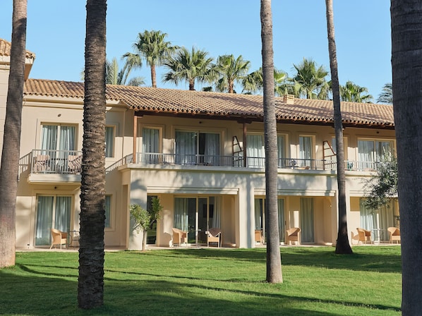 A multi-story hotel with balconies, palm trees, and a well-maintained lawn.