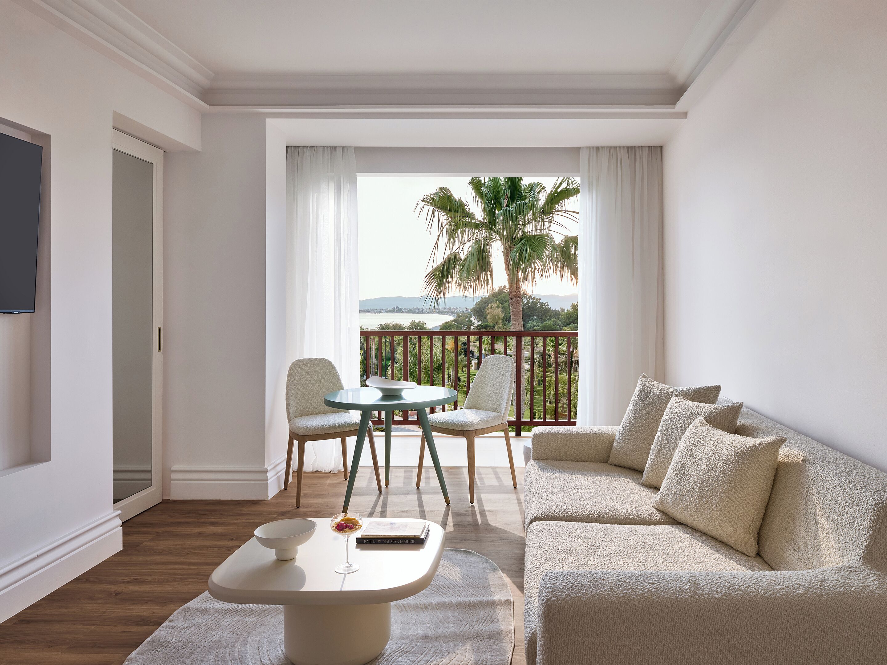 Ein modernes Hotelzimmer mit Balkon, einer Couch, einem Esstisch und einem Fernseher.