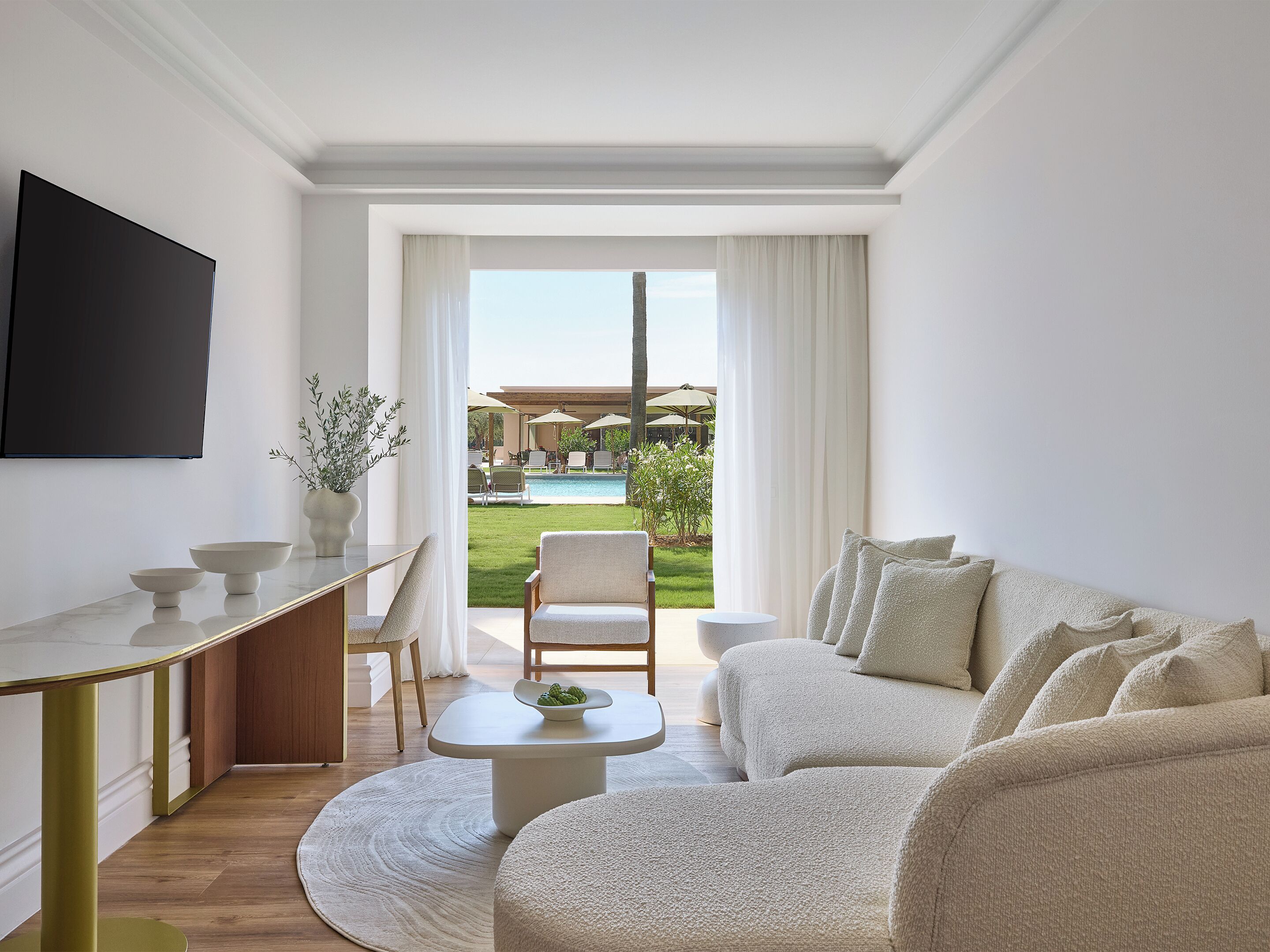 Un salon moderne comprenant un canapé, une table basse, un coin repas avec une table et des chaises, et une vue sur une piscine et un jardin.