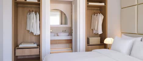 A hotel room with a large bed, a walk-in closet with wooden doors, a bathroom with a double sink, and a mirror above the sink.