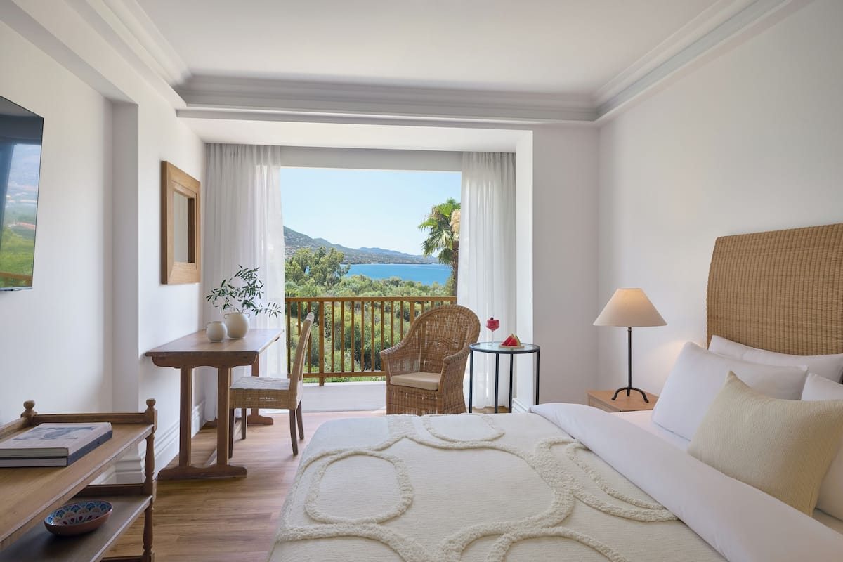 Une chambre d’hôtel avec un grand lit, une petite table avec une lampe, une chaise et une vue sur un lac et des montagnes.
