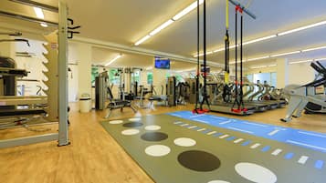 Et fitnesscenter med konditionsmaskiner, styrketræningsudstyr og en blå måtte med hvide og sorte cirkler.