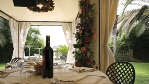 A tented outdoor dining area with a table set for a meal, surrounded by chairs and a decorative floral arrangement. - Hotel Villa Picena (Colli del Tronto)