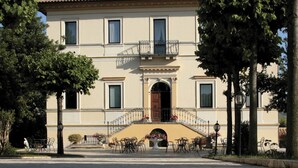 A two-story building with a symmetrical facade, a central entrance with an archway, and a balcony on the second floor. - Hotel Villa Picena (Colli del Tronto)