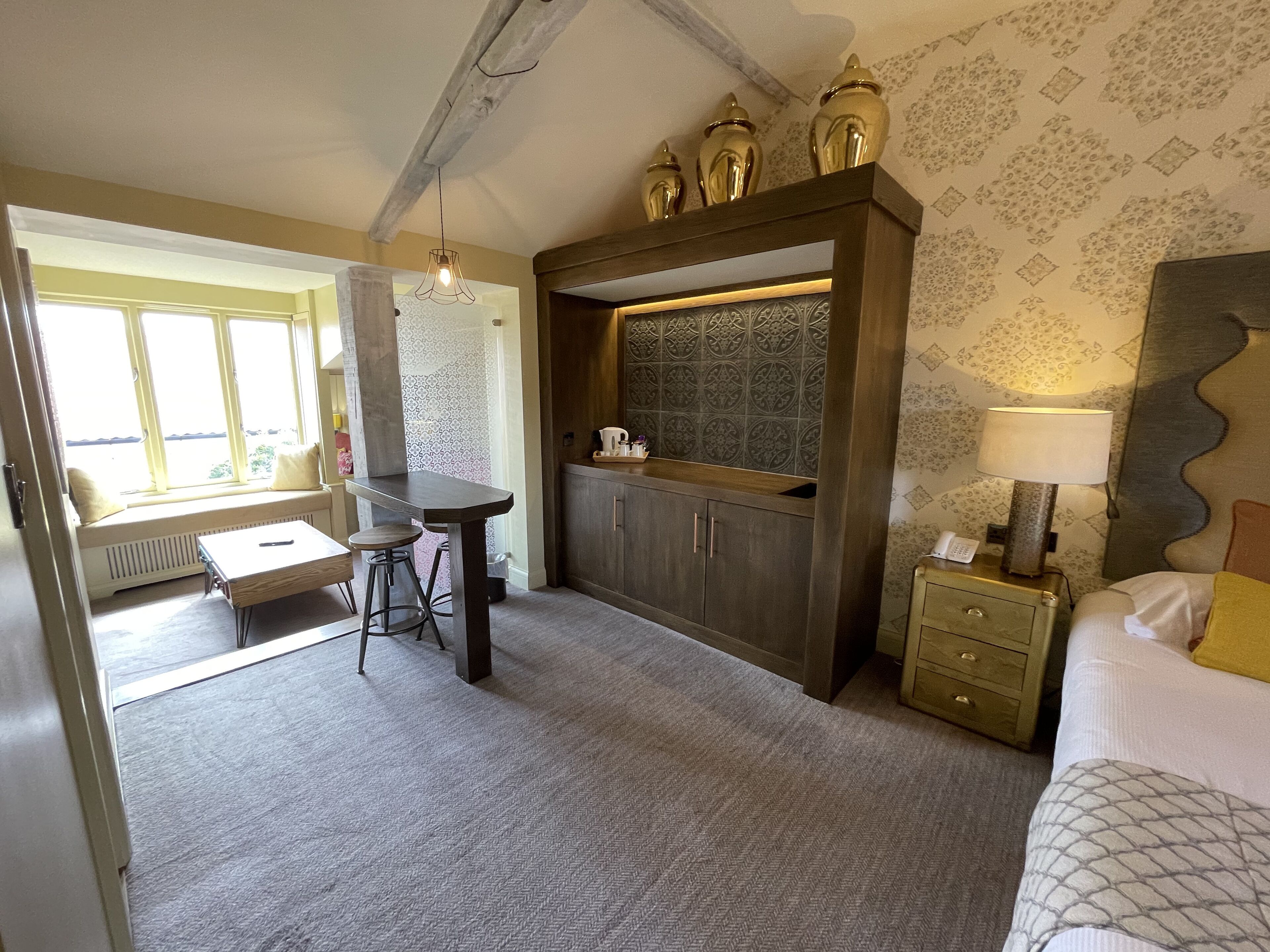 Ein Zimmer mit Esstisch, Barhocker, Küchenzeile inklusive Schränken, einem Fenster mit Aussicht und einem Bett mit gemustertem Bettbezug.