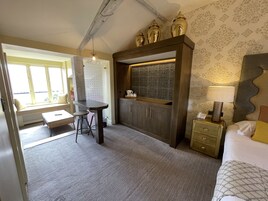 Una habitación con una mesa de comedor, taburetes de bar, una zona de cocina con armarios, un ventanal con vistas y una cama con colcha estampada.