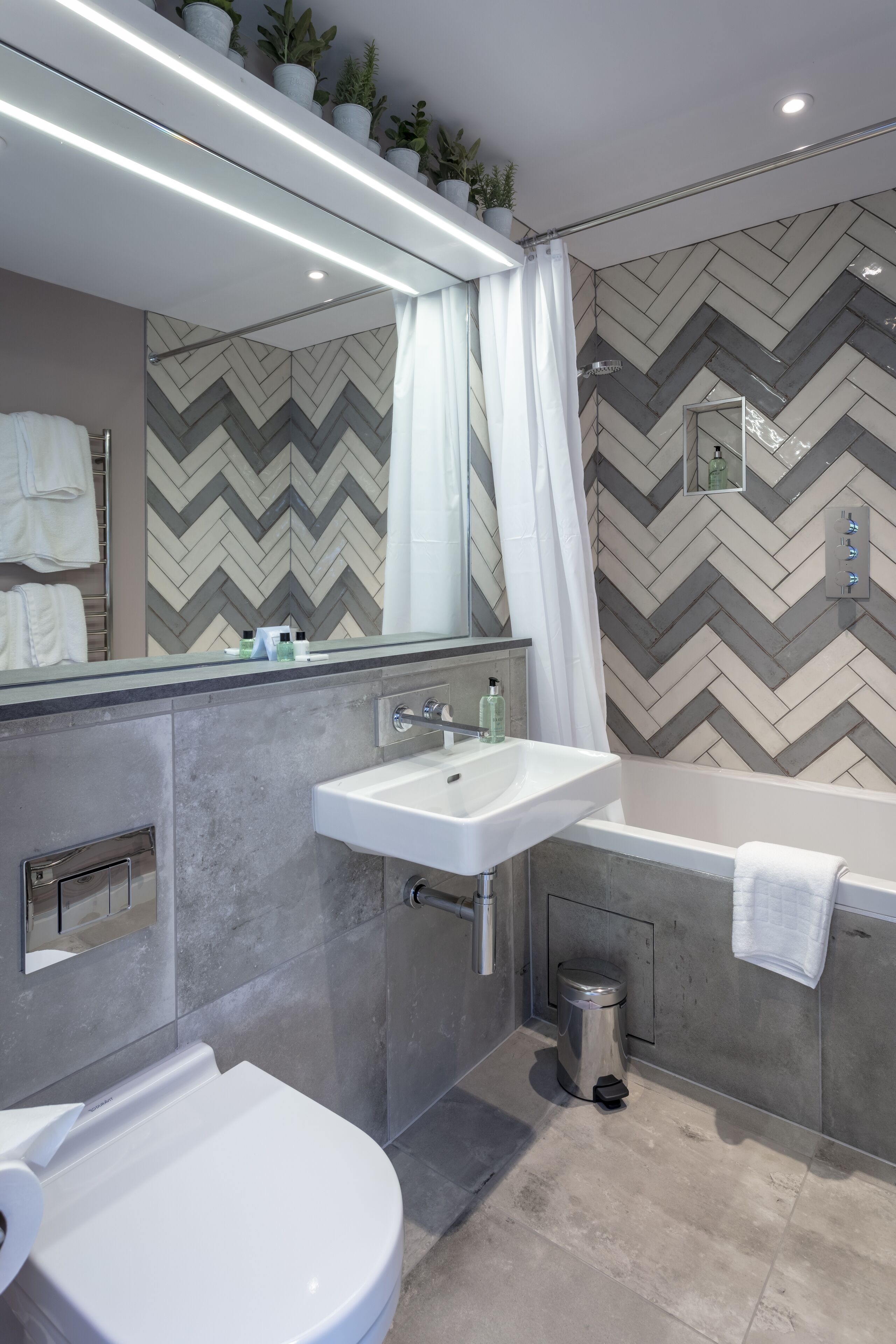 A modern bathroom with a large mirror, a sink, a toilet, and a bathtub.