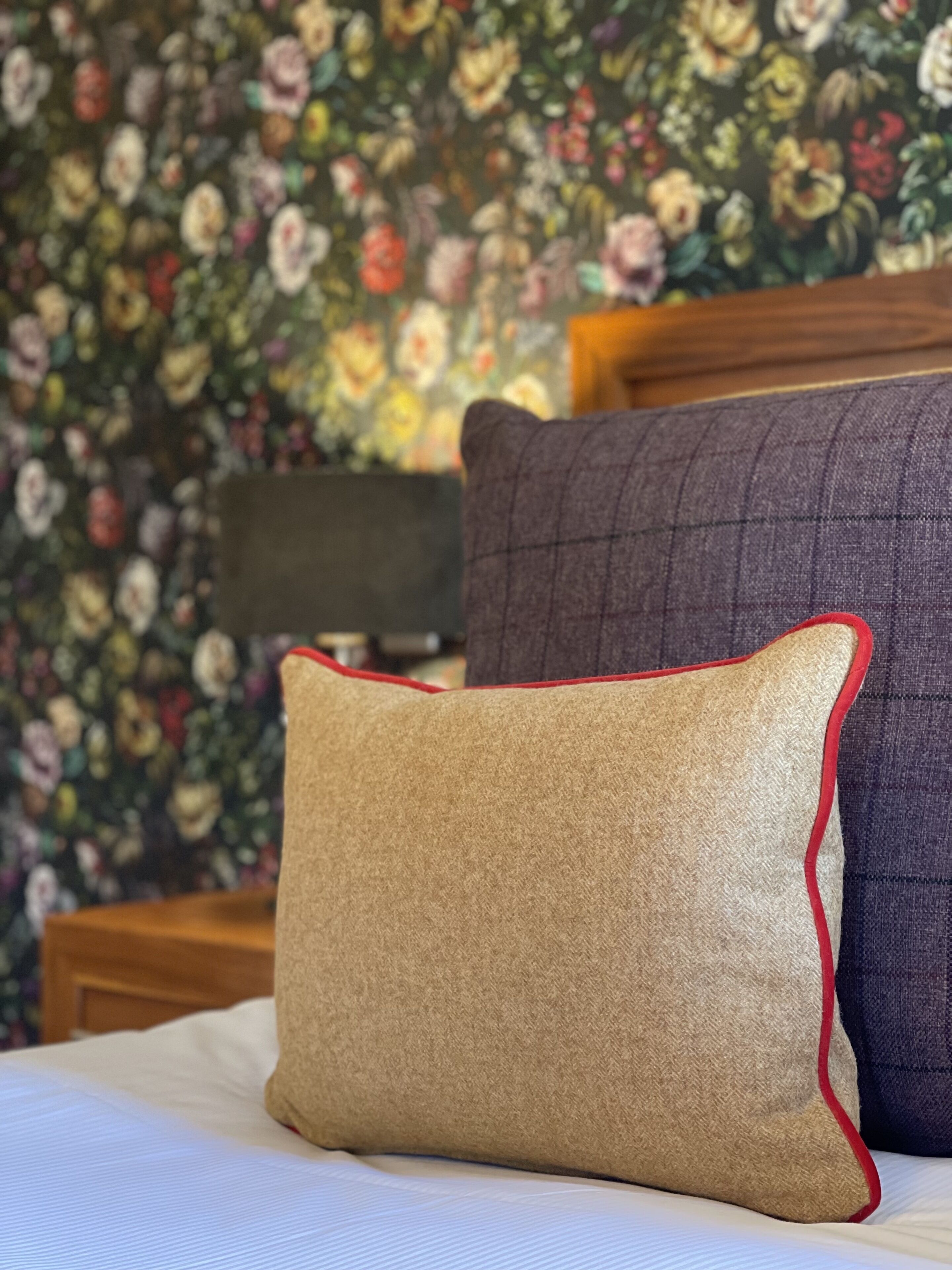A bed with a beige pillow and a dark purple pillow against a floral wallpaper background.