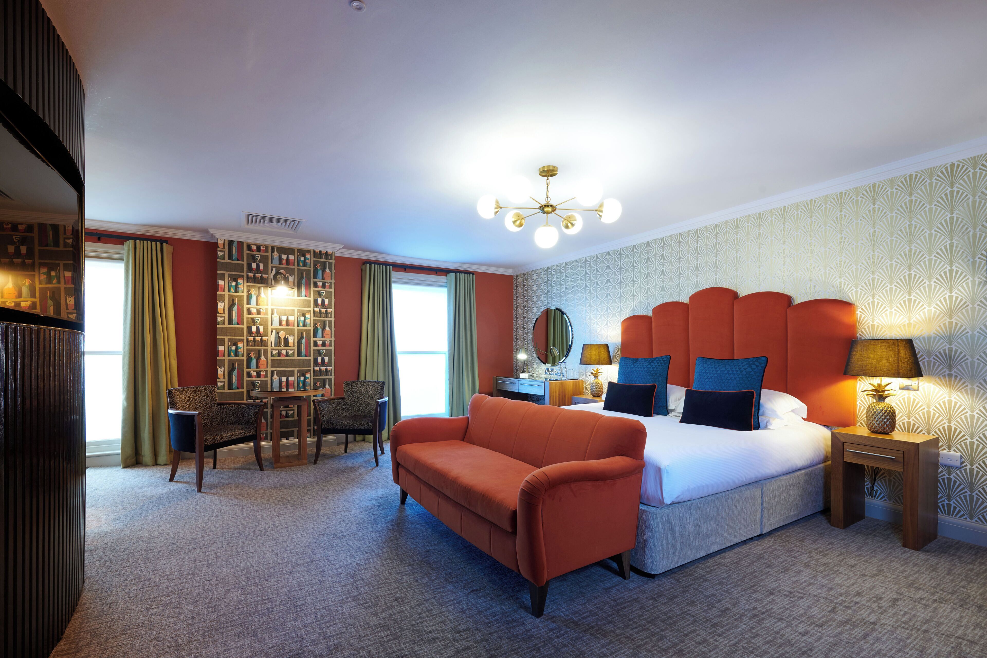 A hotel room with a large bed, a sofa, a desk, and a bookshelf.