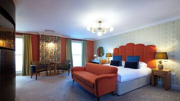 A hotel room with a large bed, a sofa, a desk, and a bookshelf.