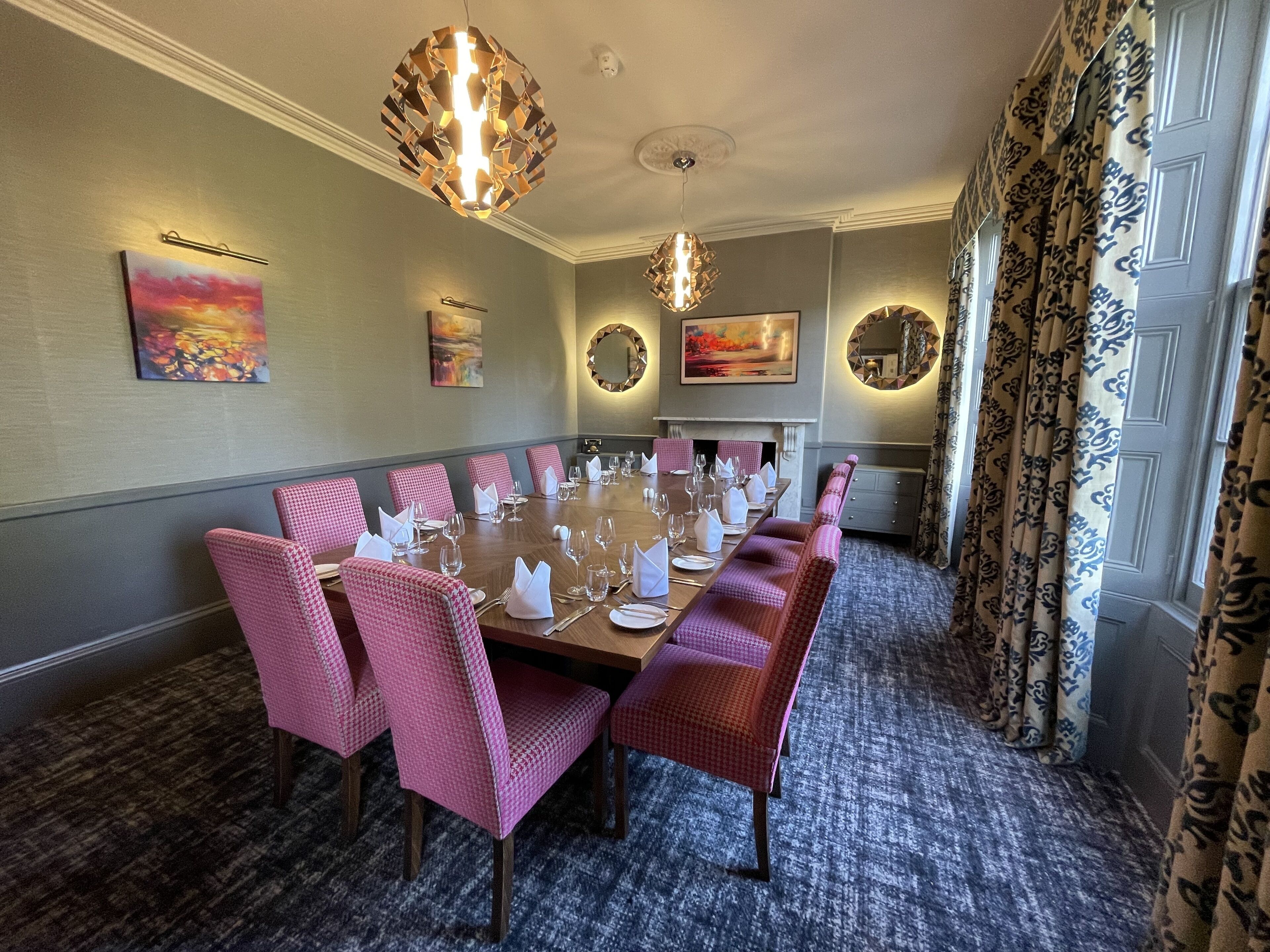 A dining room with a long table set for a meal, pink upholstered chairs, and decorative wall art.