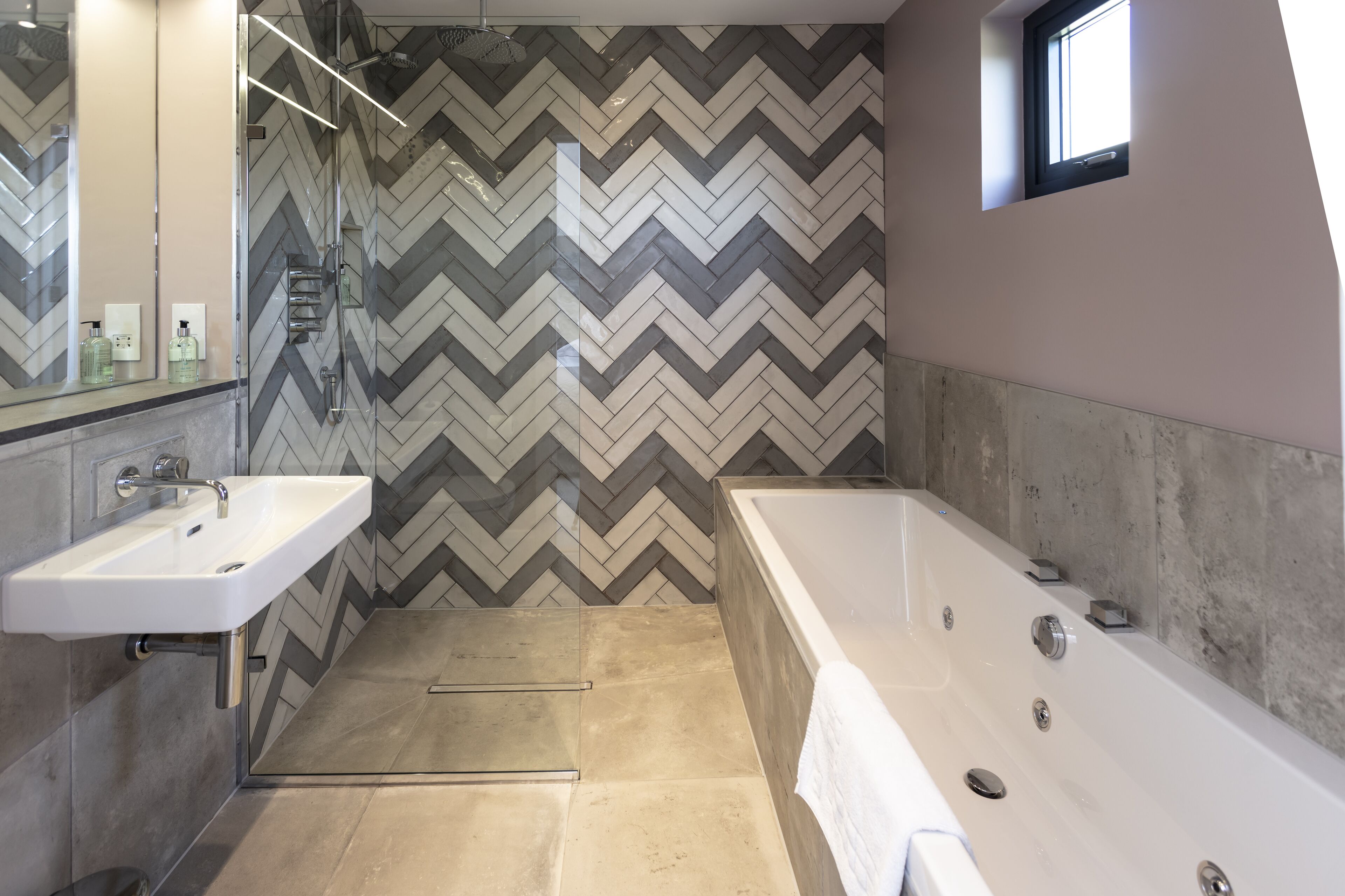 A modern bathroom with a herringbone tile backsplash, a freestanding bathtub, and a wall-mounted sink.