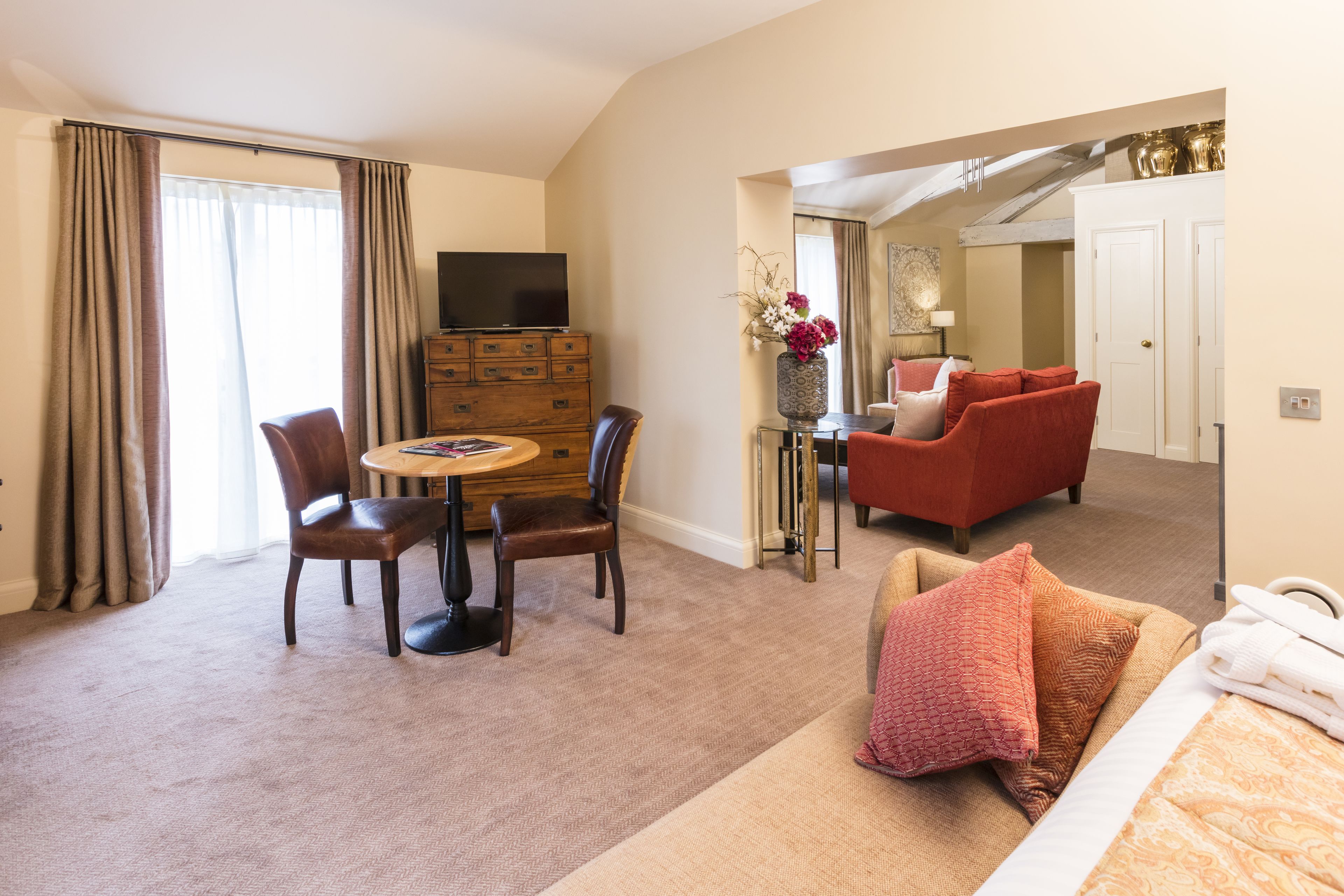 Et hotelværelse med spiseplads, sofa, TV og badeværelse, der ses gennem en åben dør.