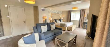 A hotel room with a large bed, a sofa, a coffee table, and a TV.