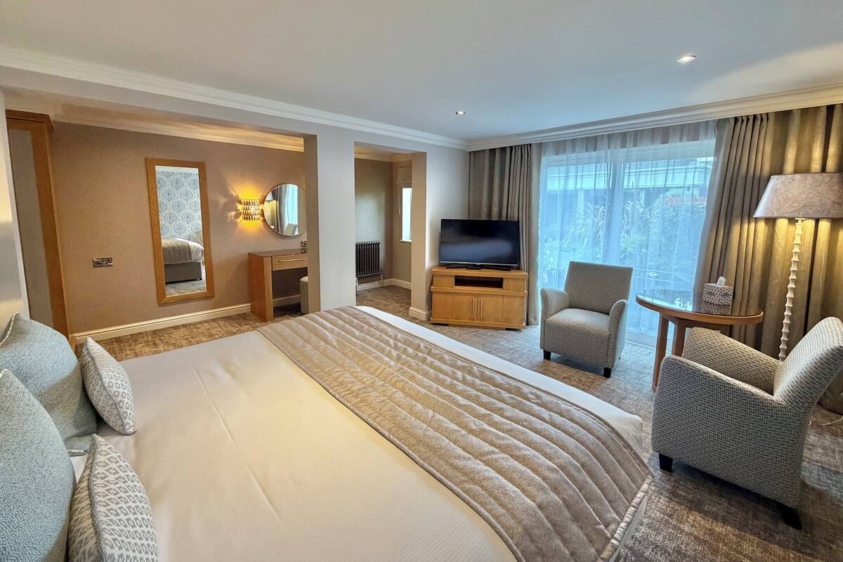 Een hotelkamer met een groot bed, een televisie, een zithoek met stoelen en uitzicht op het groen.