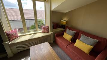 A cozy living room with a red sofa, a wooden coffee table, and a window with a view of a red-tiled roof.