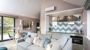 Een moderne woonkamer met een grijze bank, een eettafel en een keuken met een gegolfd achterwandpaneel.