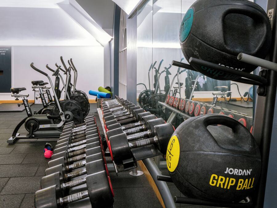 Un gimnasio con diversos equipos de ejercicio, incluyendo mancuernas, una pesa rusa y bicicletas estáticas.