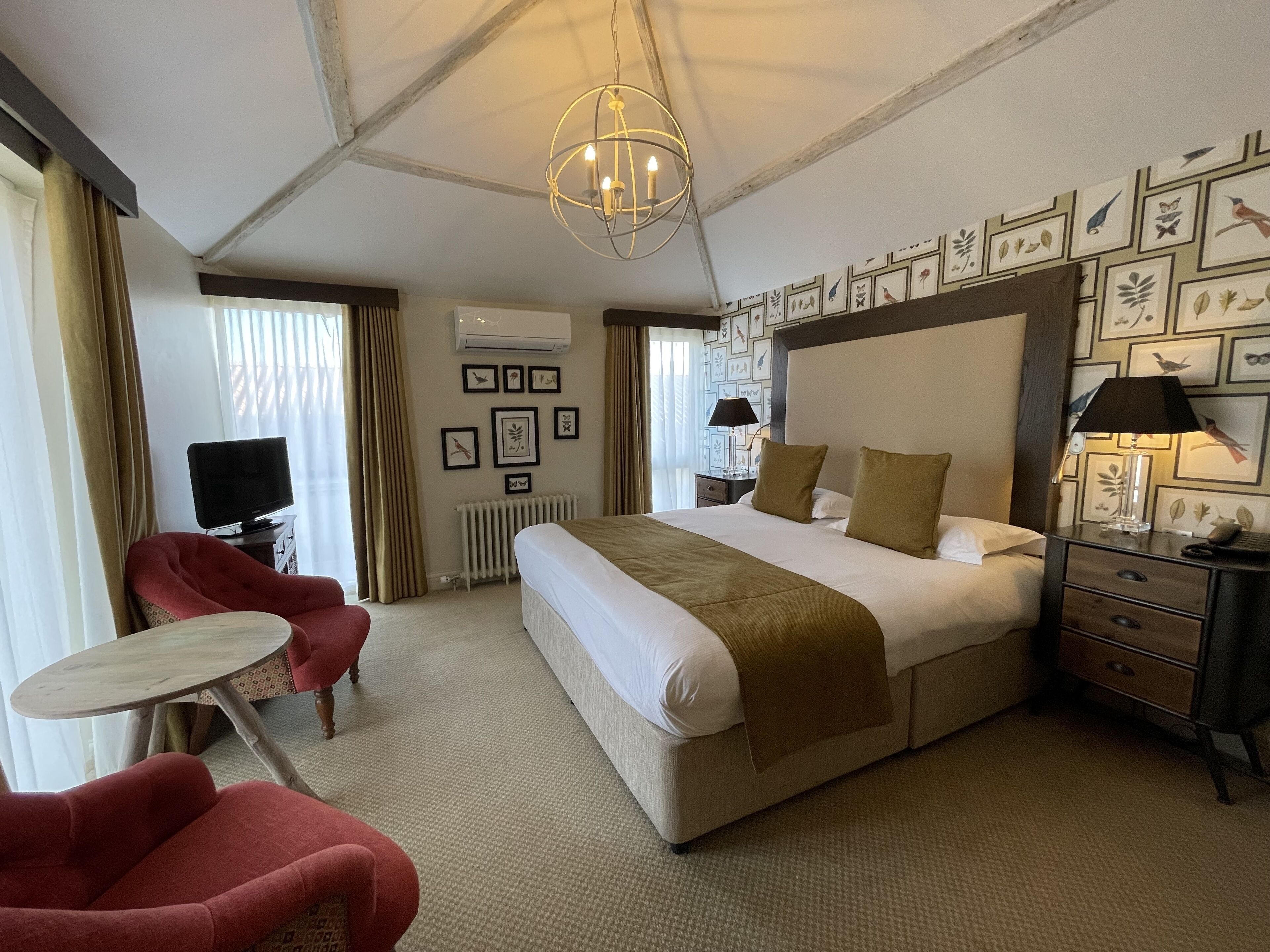 A hotel room with a large bed, a desk, a chair, and a ceiling light.