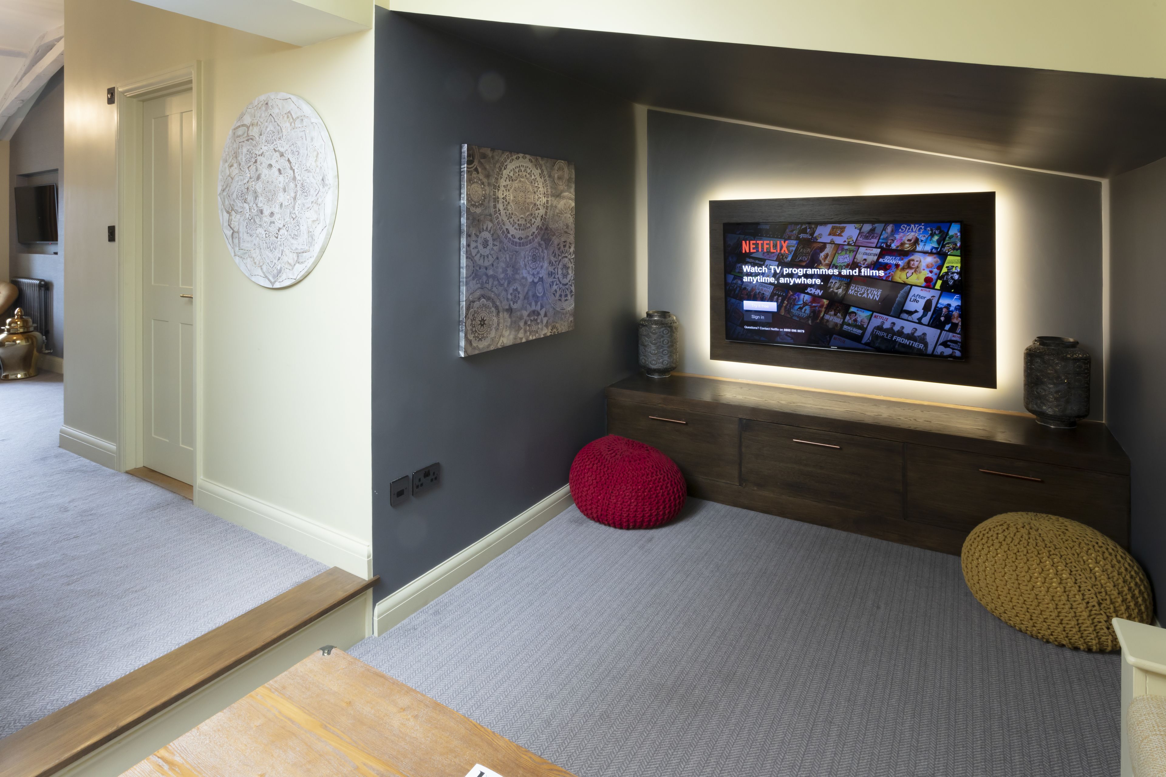 Un salón moderno con un televisor de pantalla plana montado en la pared, una mesa de centro de madera y una alfombra gris.
