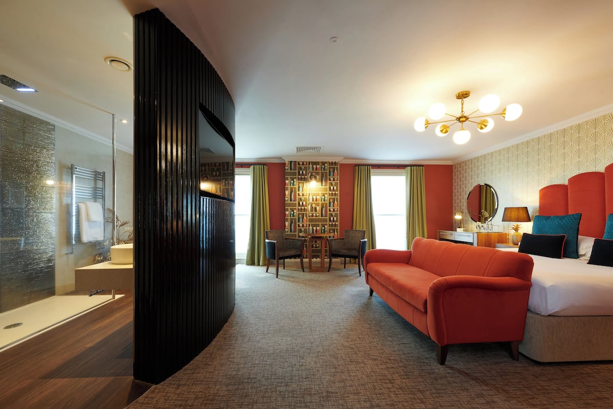 Een hotelkamer met een modern design, met een groot bed, een sofa, een zithoek met een kroonluchter en een boekenkast.