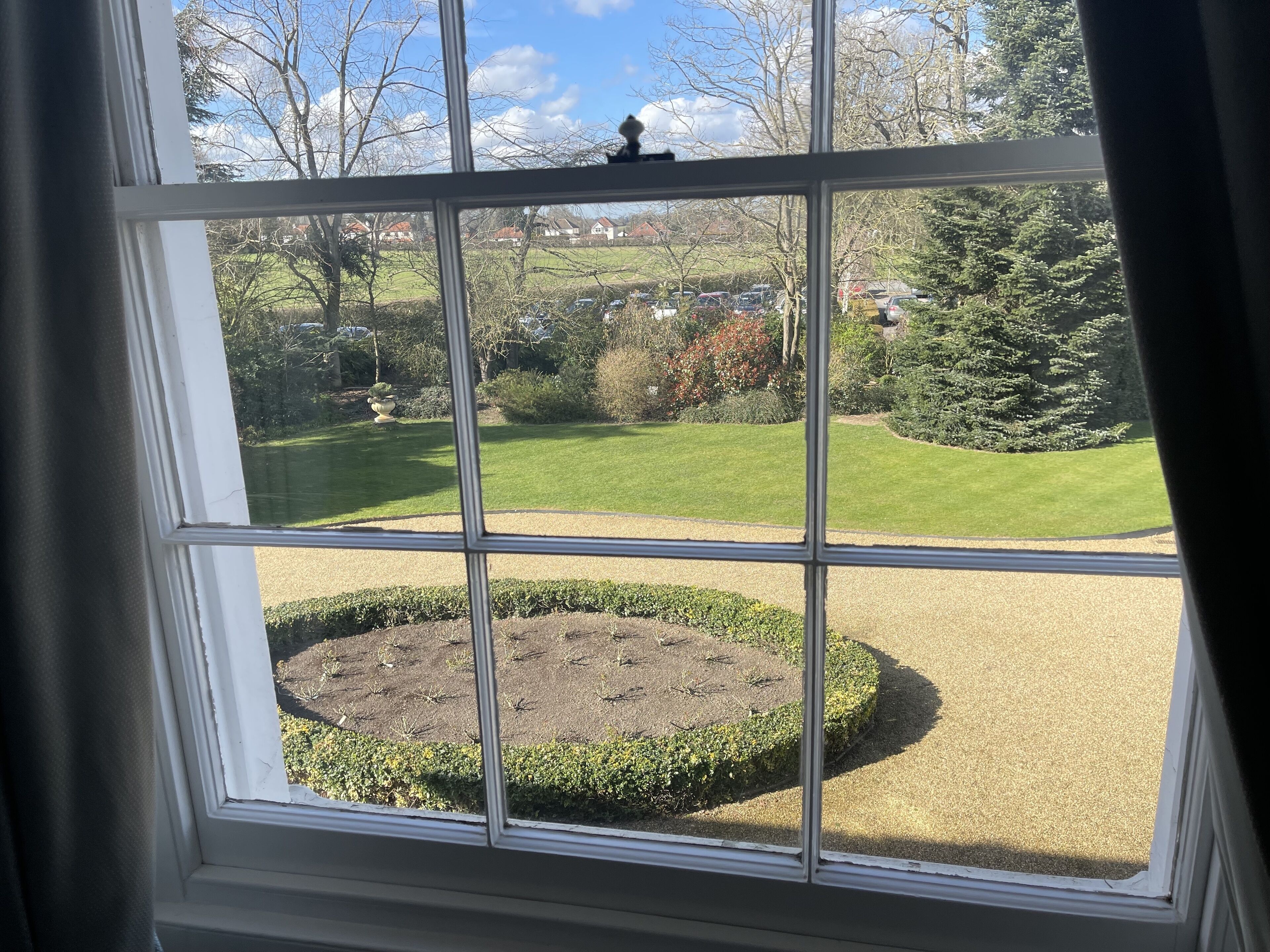 A view through a window with a garden in the foreground and houses in the background.