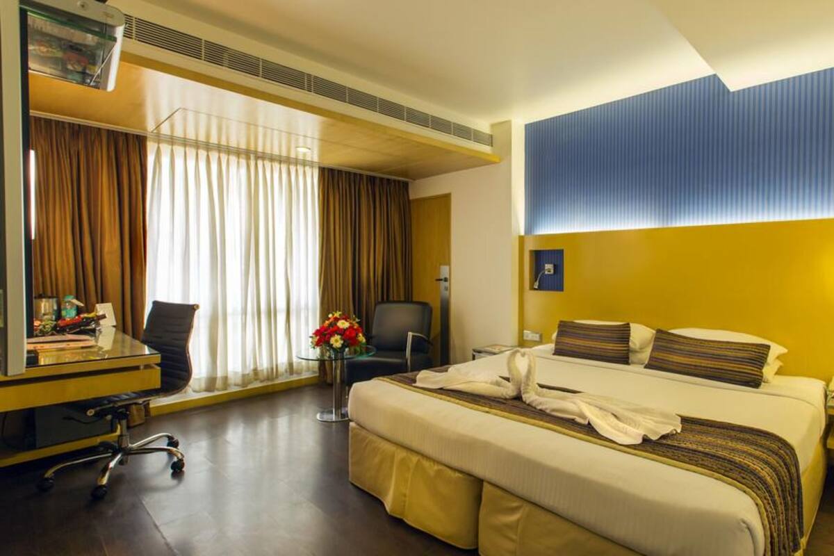 Habitación de hotel con cama, escritorio, silla y un amplio ventanal con cortinas.