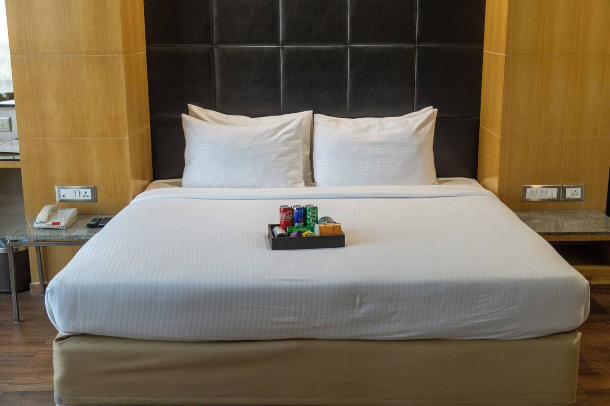 Una cama bien hecha con sábanas blancas, una bandeja con aperitivos y un teléfono en la mesita de noche.