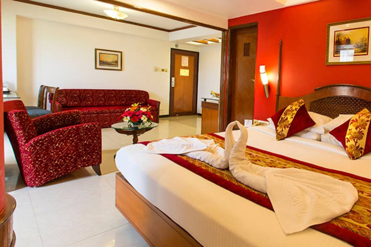 Una habitación de hotel con una cama grande, un sofá rojo, una mesita con flores y un cabecero de madera.