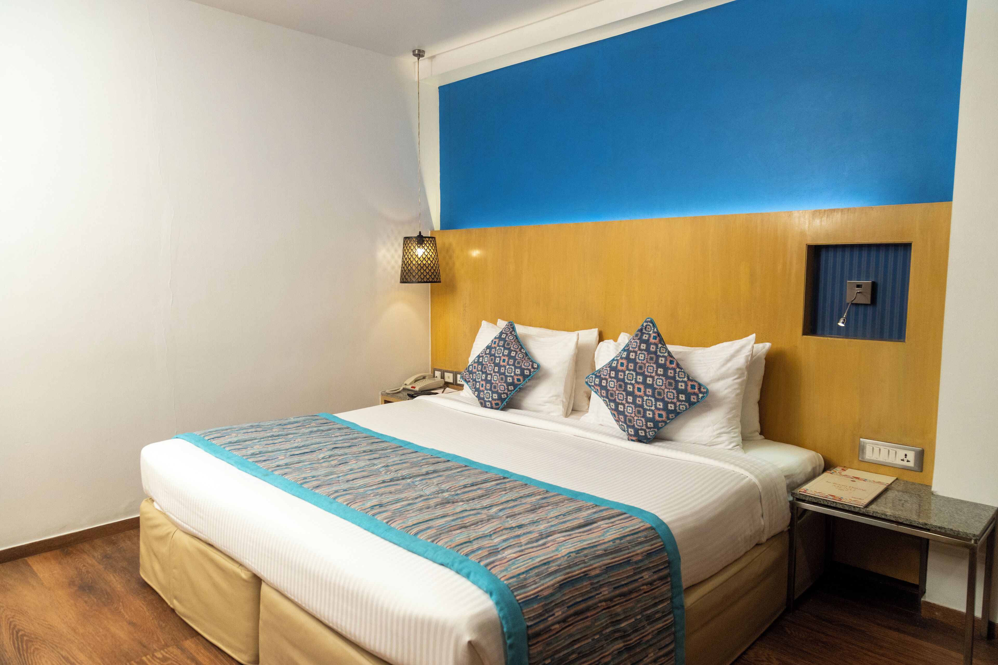 Habitación de hotel con una cama grande, una mesita de noche, una lámpara de pared y un cabecero de madera.