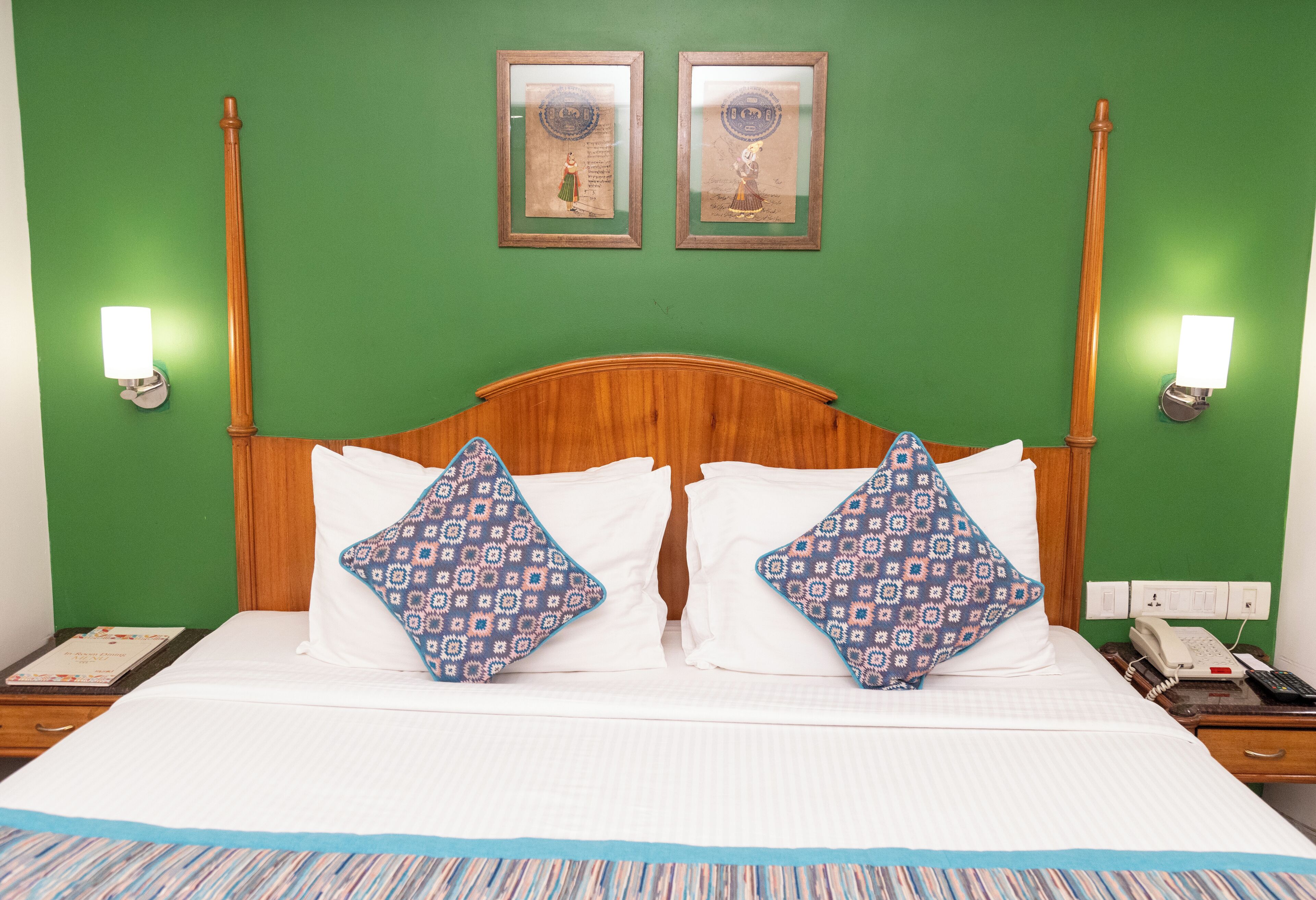 A hotel room with a wooden headboard, two patterned pillows, a striped area rug, and two framed pictures on the wall.