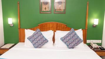 A hotel room with a wooden headboard, two patterned pillows, a striped area rug, and two framed pictures on the wall.