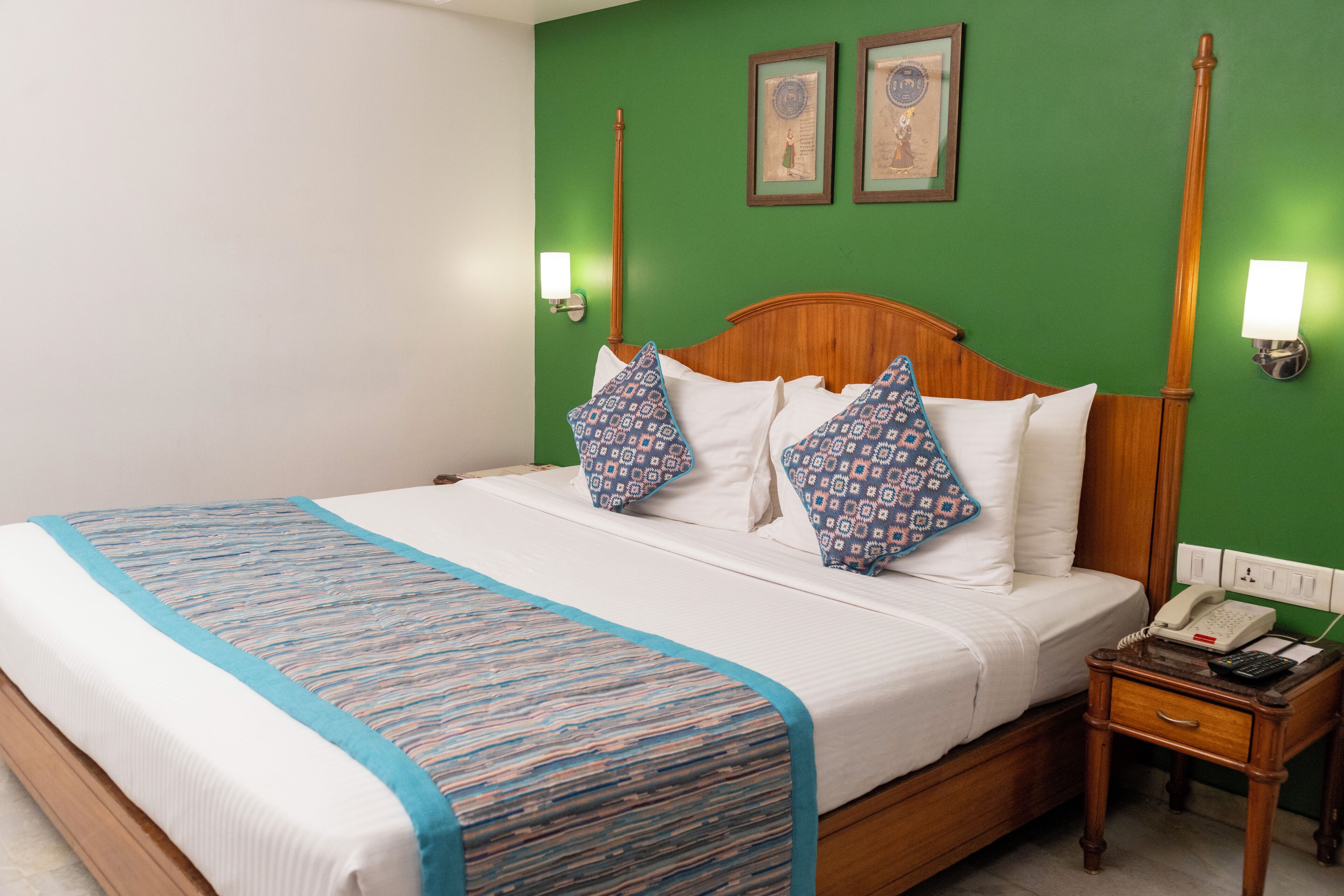 Une chambre d’hôtel avec un grand lit, une tête de lit en bois, deux lampes fixées au mur et une table de chevet avec un téléphone.
