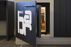 Eine Tür mit einem großen Schild, auf dem 'mini' steht, und einem Griff, die zu einem Raum führt, in dem sich ein Kühlschrank und eine Orange befinden.